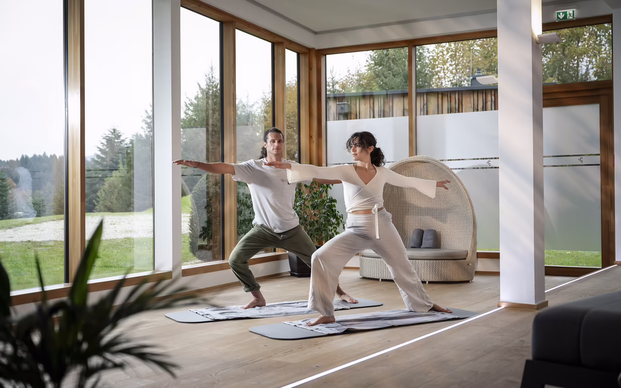 Zwei Personen beim Yoga in einem hellen Raum mit großen Fenstern im DAS SIEBEN