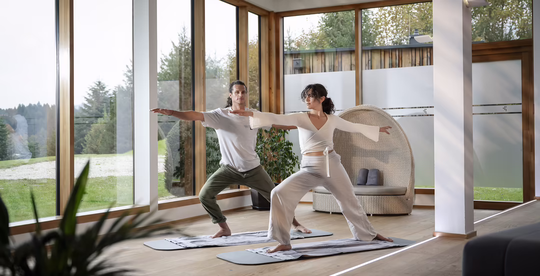 Zwei Personen beim Yoga in einem hellen Raum mit großen Fenstern im DAS SIEBEN