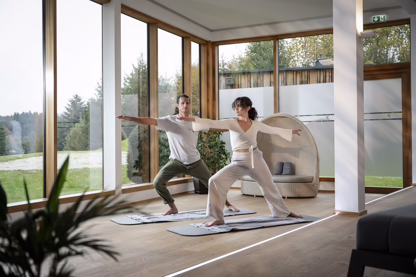Zwei Personen beim Yoga in einem hellen Raum mit großen Fenstern im DAS SIEBEN