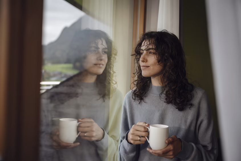 Frau mit Tasse auf einem Balkon mit Blick auf Berge und Landschaft im DAS SIEBEN