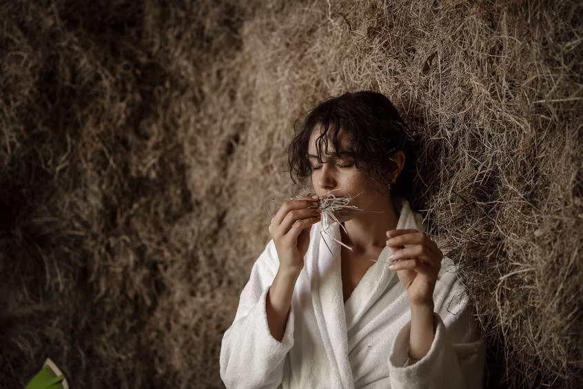 Frau im Bademantel riecht an Heu in einem Ruheraum bei DAS SIEBEN