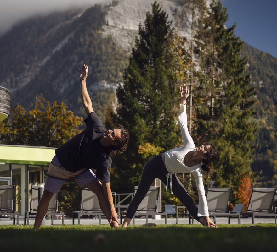 Zwei Personen machen Yoga auf einer Wiese vor dem Hotel DAS SIEBEN
