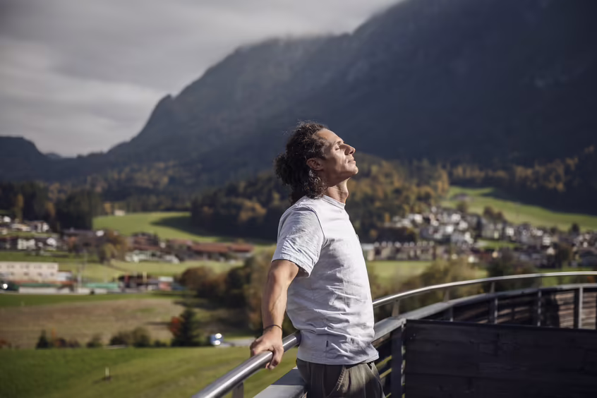 Mann atmet auf einer Terrasse mit weitem Blick auf Berge und Landschaft im DAS SIEBEN durch