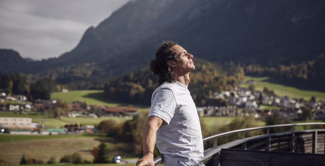Mann atmet auf einer Terrasse mit weitem Blick auf Berge und Landschaft im DAS SIEBEN durch