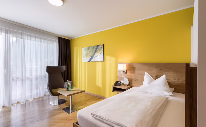 Freundliches Einzelzimmer mit gelber Wand, Holzboden und großem Fenster