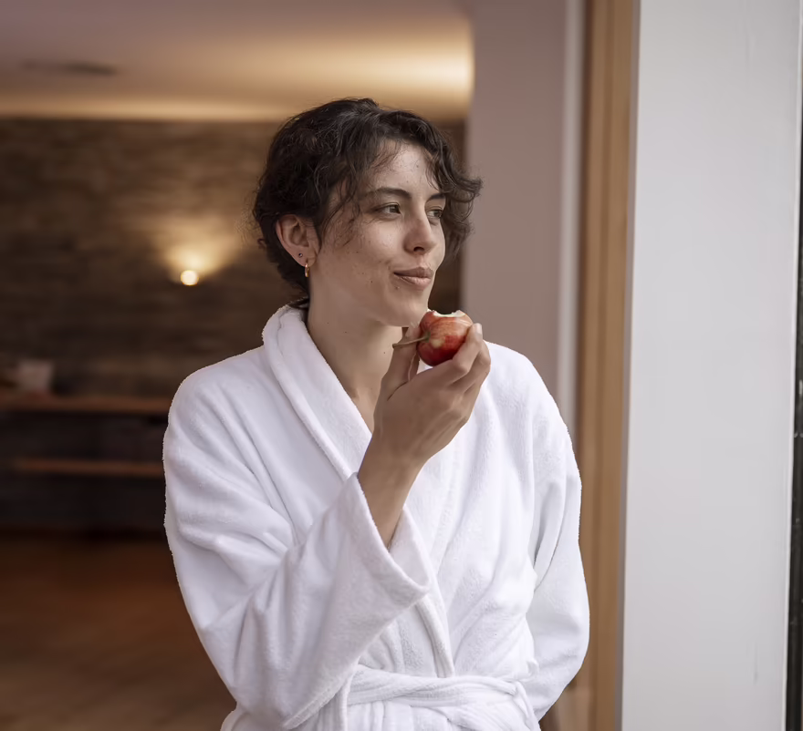 A woman in a bathrobe in the DAS SIEBEN wellness area is enjoying an apple